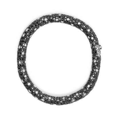 Top-down view of a white metal bracelet encrusted with round black and white gemstones in a prong setting.