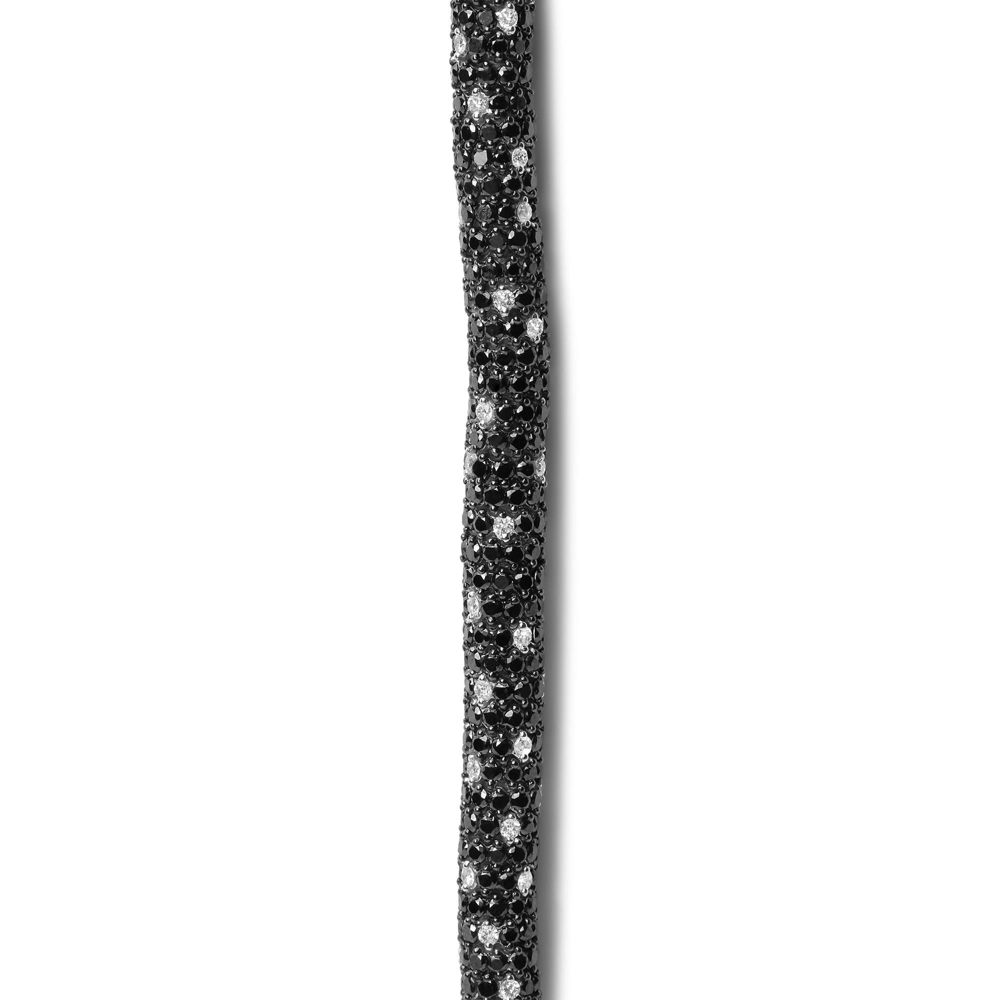 Close-up side view of a white metal bracelet paved with round black and white gemstones in prong settings.