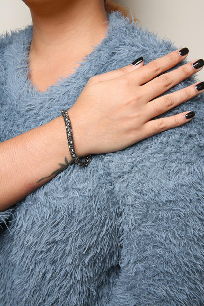 White metal bracelet with black and white round gemstones in prong settings, shown on a model's wrist, angled from the side.