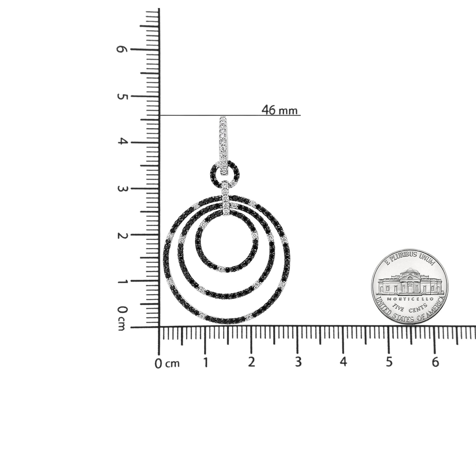 Top view of a white metal earring with three concentric circular hoops pavé set with alternating black and white round gemstones, shown on a ruler and next to a coin for size reference.
