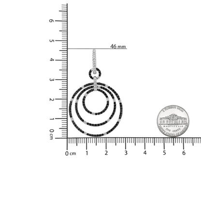 Top view of a white metal earring with three concentric circular hoops pavé set with alternating black and white round gemstones, shown on a ruler and next to a coin for size reference.
