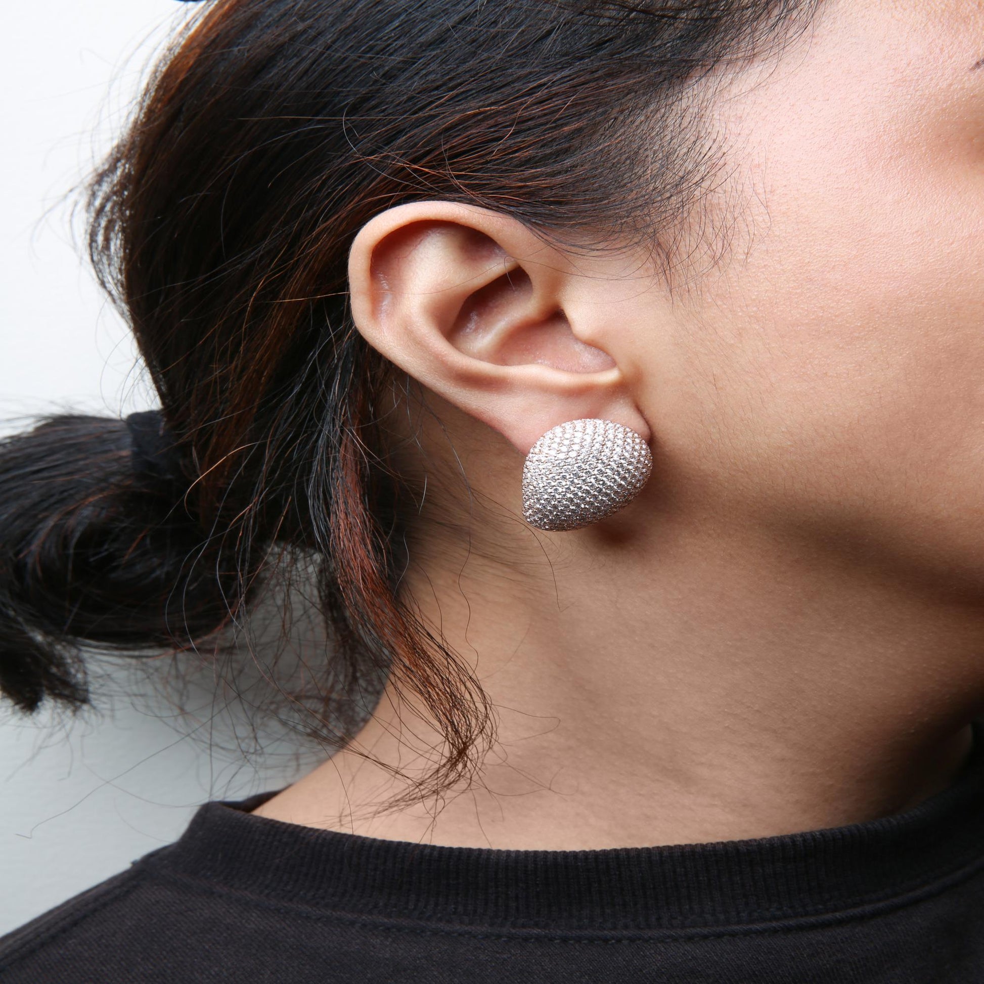 Close-up side view of a model wearing rose-colored earrings studded with numerous small white gemstones in a pave setting.