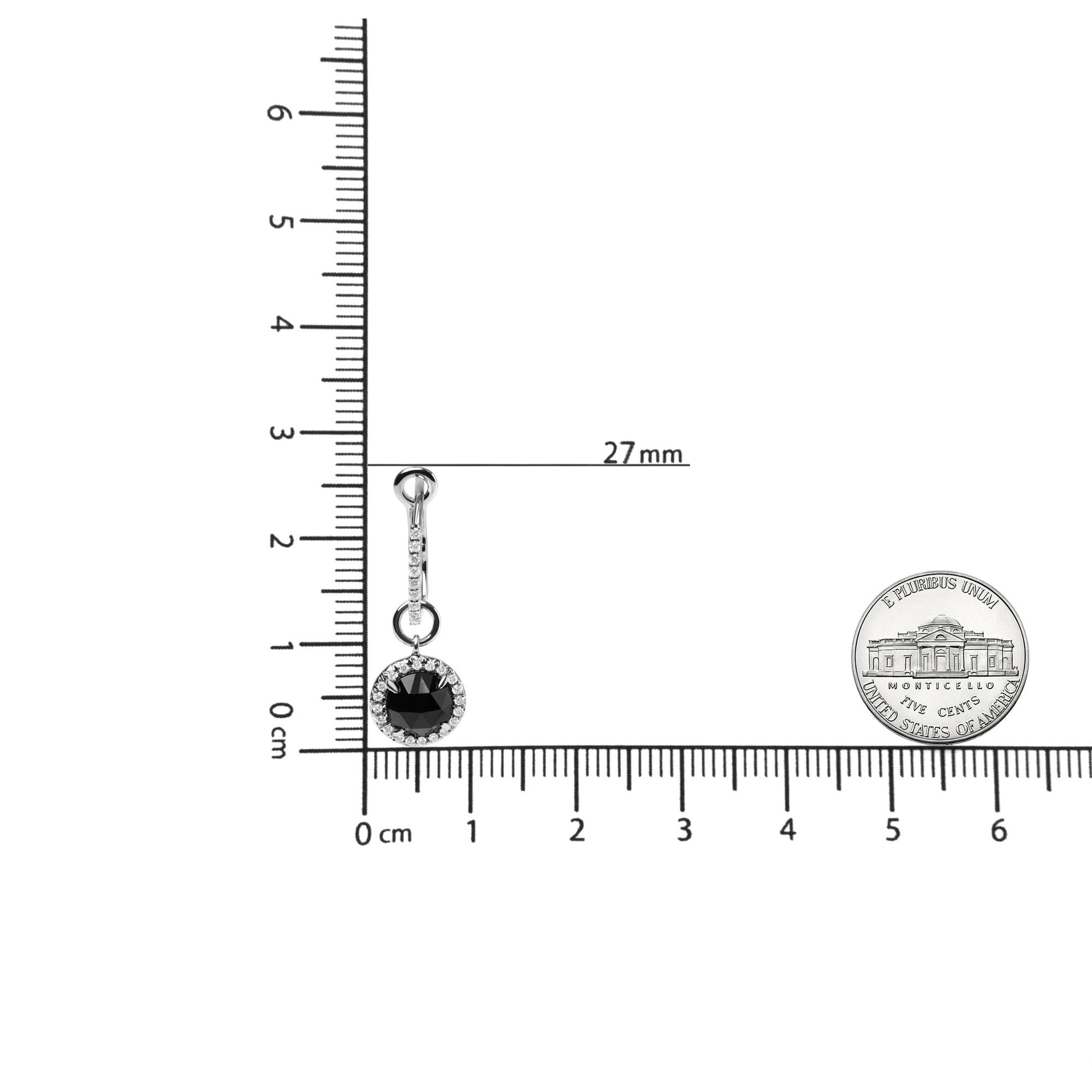 Single white metal earring with a round black gemstone surrounded by small white gemstones, shown on a ruler for size reference, viewed from the front.