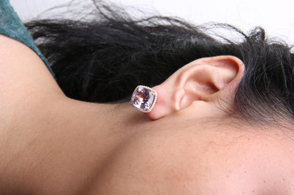 Close-up side view of a white and rose metal earring with a cushion-shaped pink gemstone surrounded by small round white gemstones, worn on a model's ear.