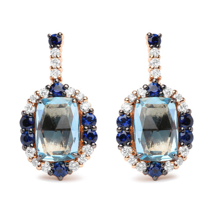 Pair of drop earrings photographed from the front, featuring large cushion-shaped blue gemstones surrounded by round blue and white gemstones, set in white and rose-colored metal.