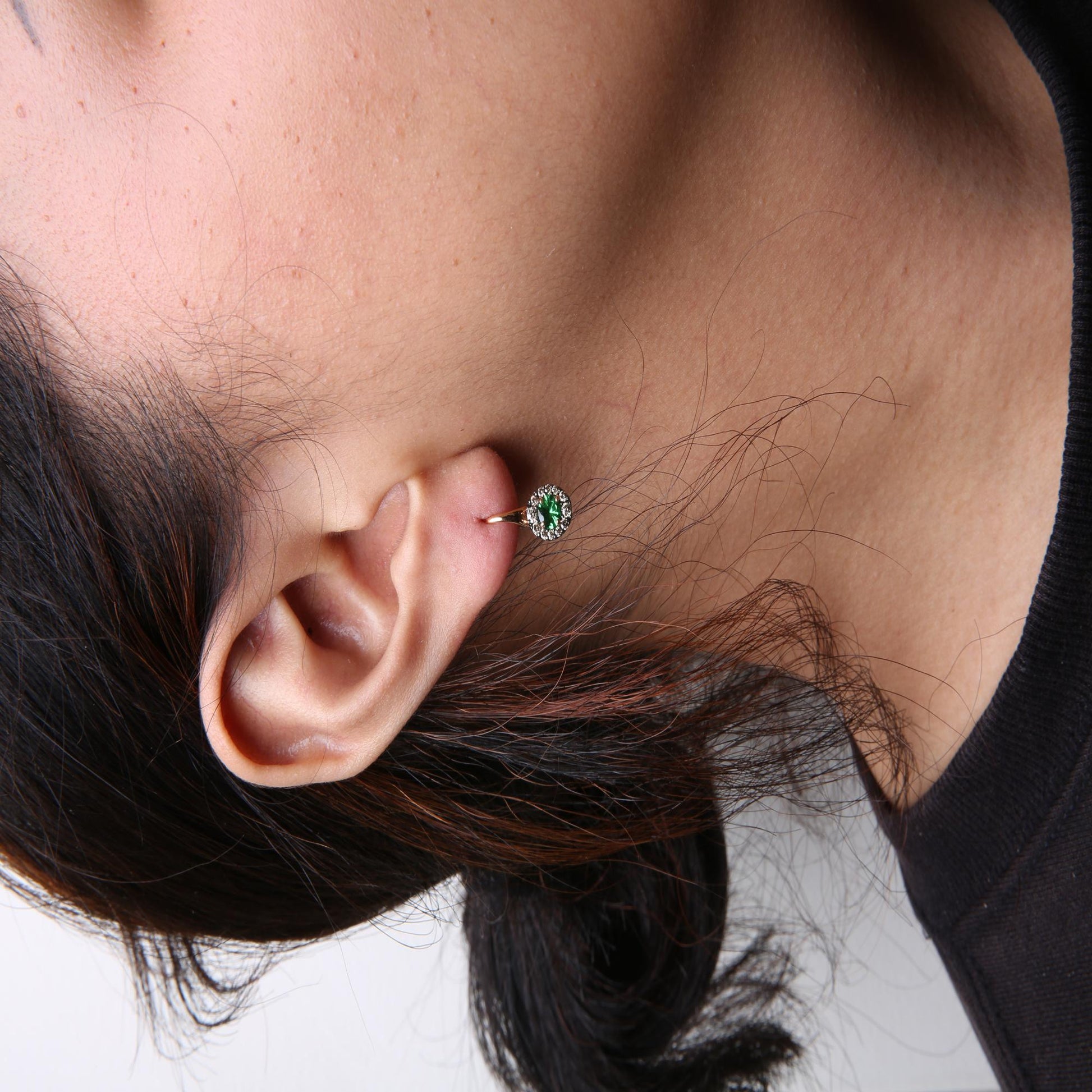 Close-up side view of a model wearing white and rose metal earrings featuring a central round green gemstone surrounded by small round brown gemstones in prong settings.