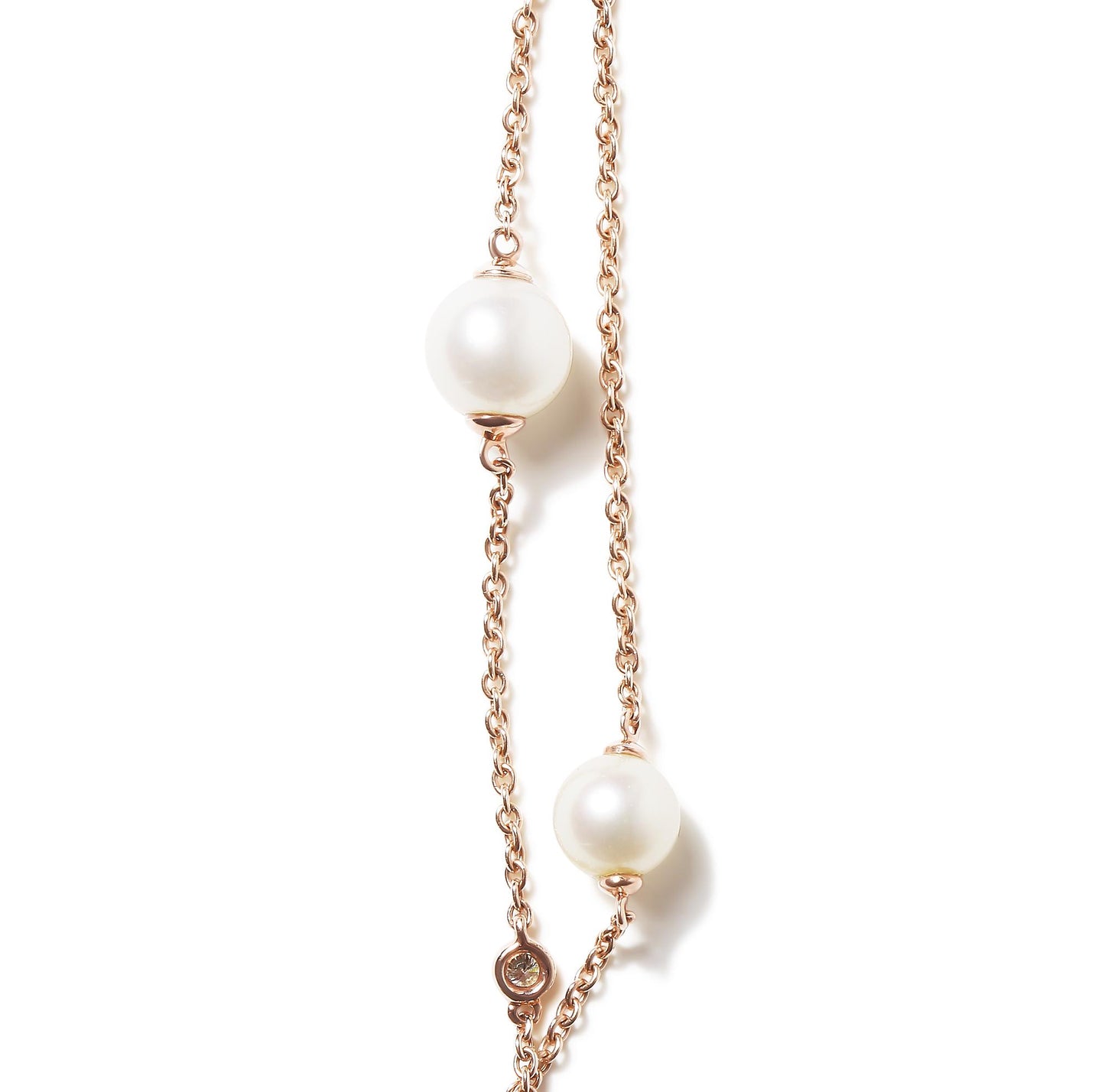 Close-up angled shot of a rose-colored metal necklace featuring round white gemstones in bezel settings and two large white pearls.