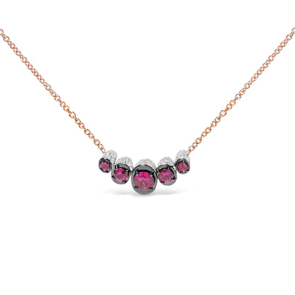 Front view of a rose metal necklace featuring a curved row of round red gemstones in prong settings, accented with small round white gemstones in pave settings.