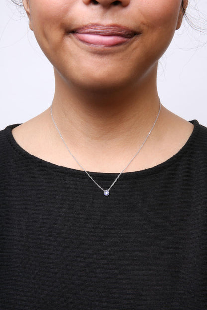 Close-up front view of a white metal necklace with a pendant featuring one white gemstone surrounded by blue gemstones, worn on a model with a black top.