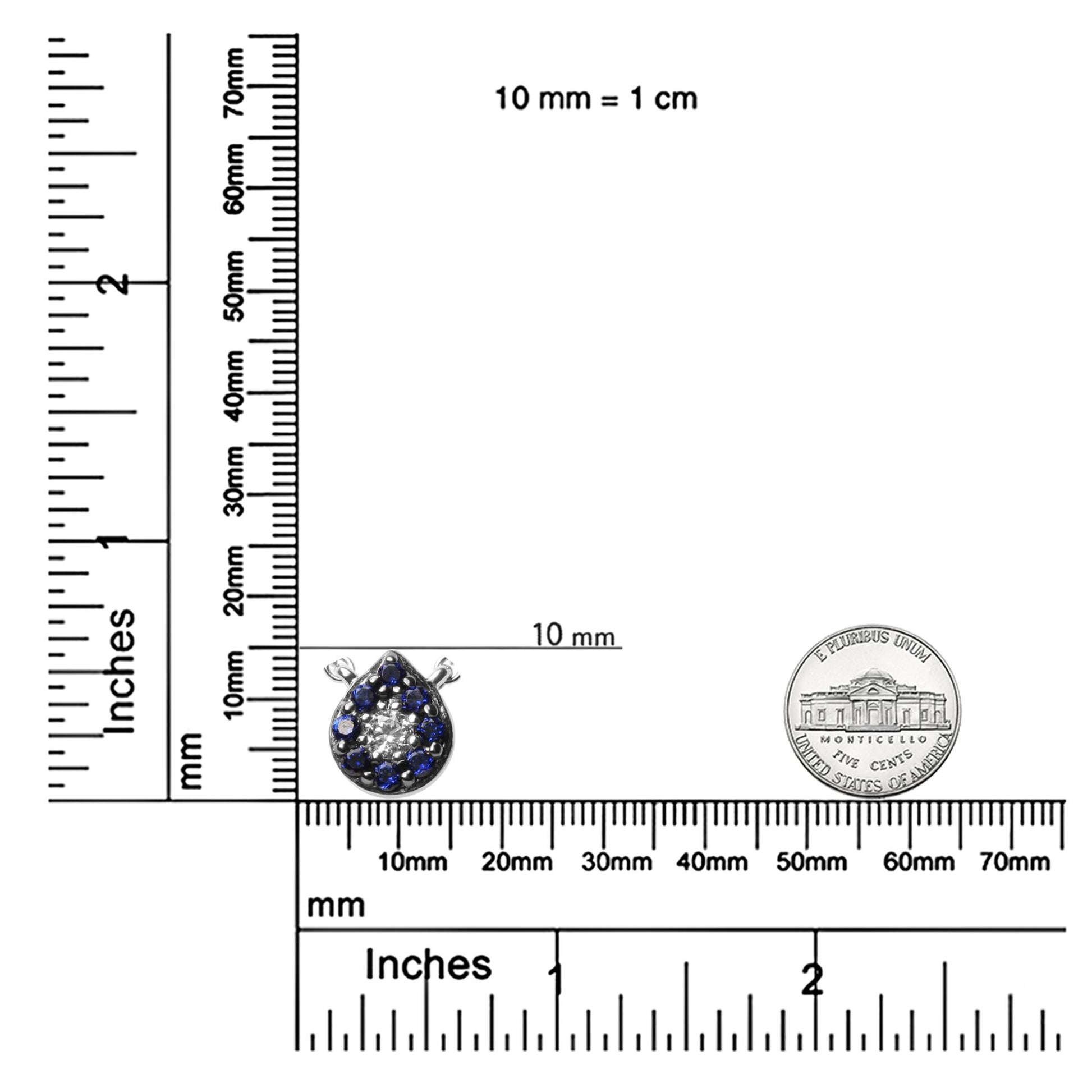 White metal necklace pendant with round white gemstone center surrounded by round blue gemstones in prong setting, shown on a ruler and scale for size reference, top-down angle.
