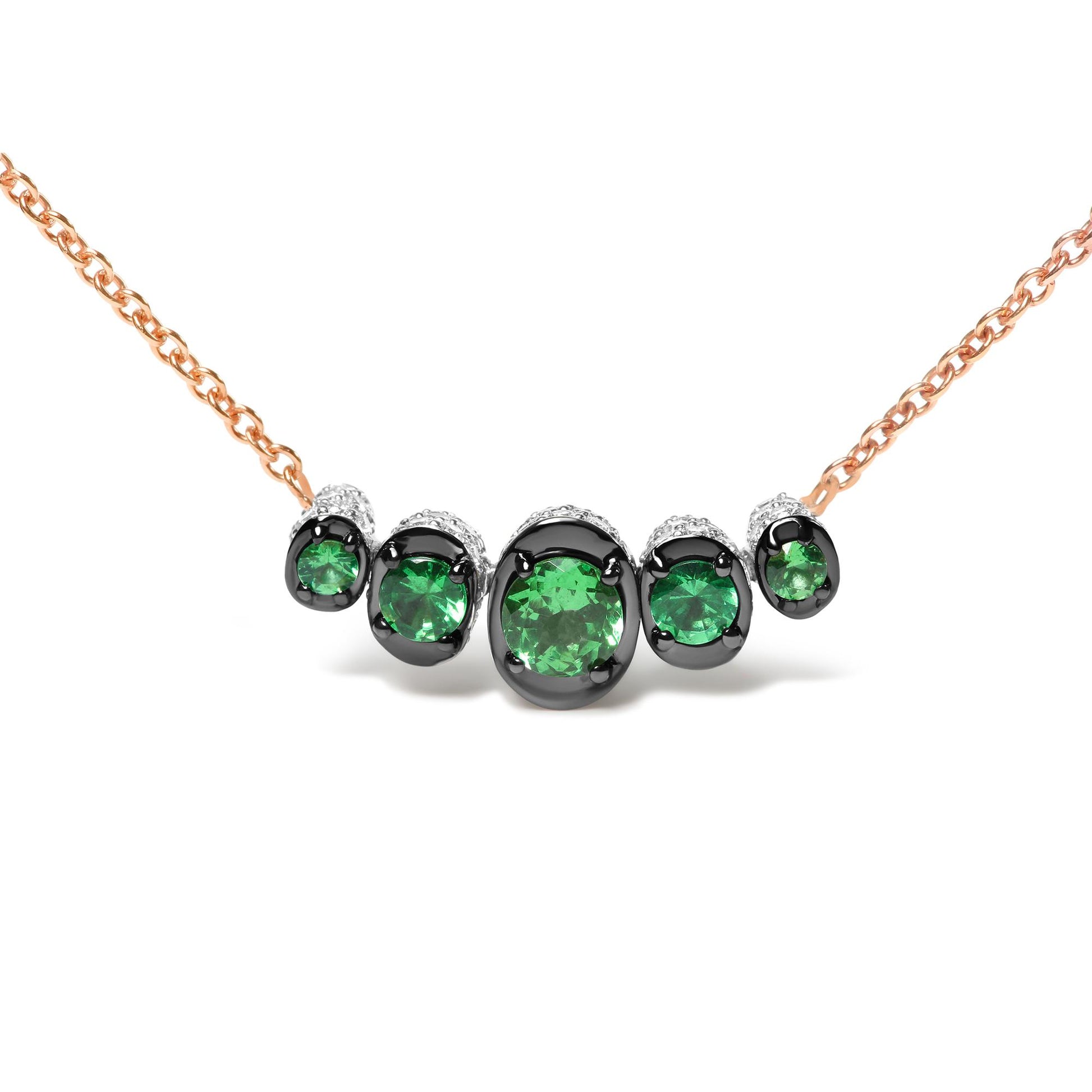 Front view of a rose metal necklace with round green gemstones in black prong settings and small white gemstones surrounding them.