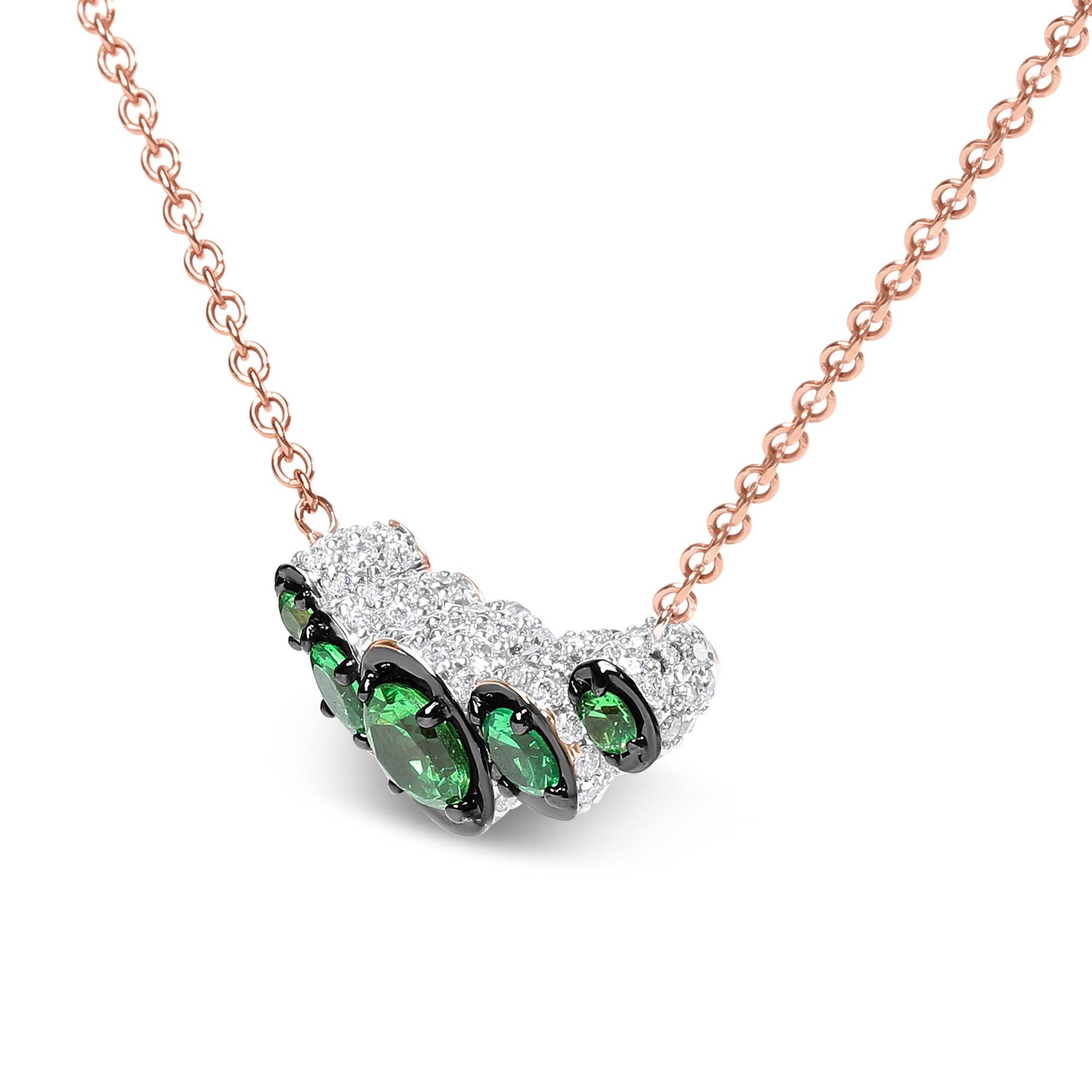 Close-up front angle of a rose metal necklace with a curved pendant featuring multiple round white gemstones and a cluster of round green gemstones in prong settings.