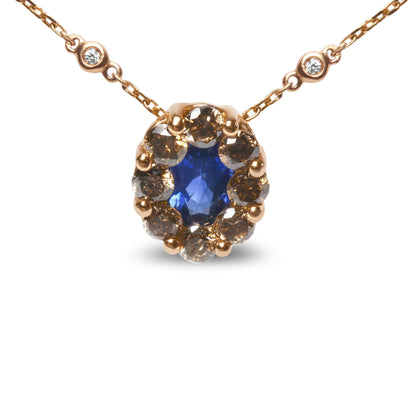 Front view of a rose metal necklace with an oval blue gemstone surrounded by round brown gemstones, and accented by two round white gemstones on the chain.