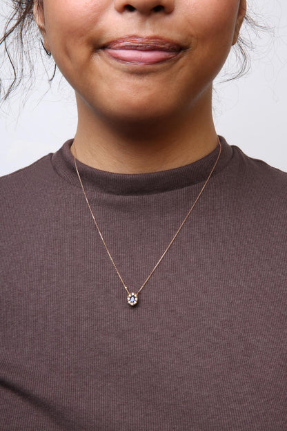 Front view of a rose metal necklace with a pendant featuring a central blue oval-shaped gemstone surrounded by round brown gemstones and two white round gemstones, worn on a model with a brown ribbed top.
