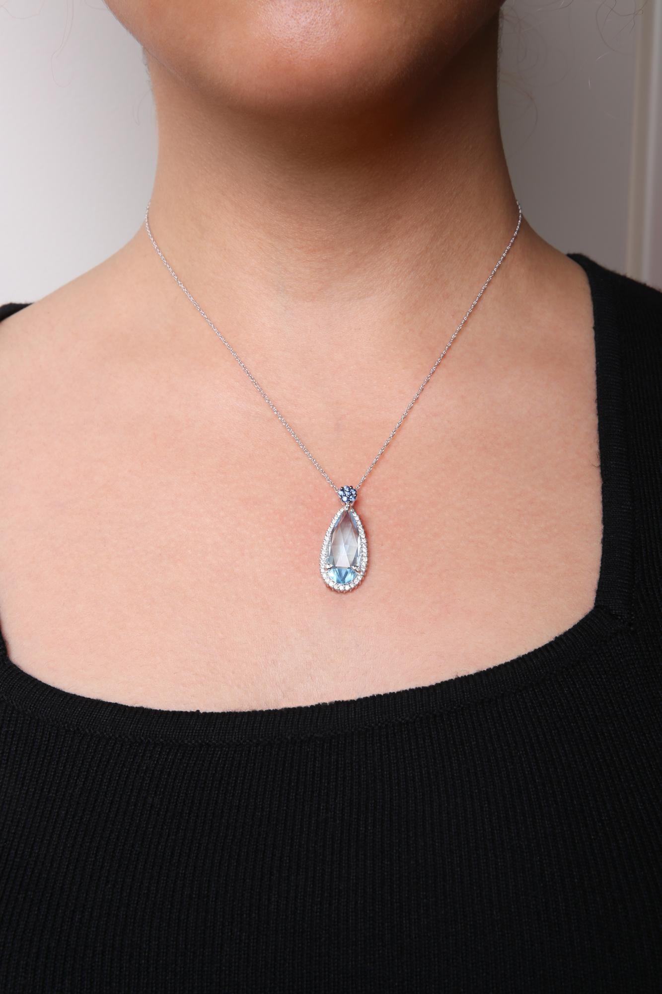 White metal necklace with a pear-shaped blue gemstone pendant surrounded by white gemstones, accented with small blue round gemstones, shown on a model from the front.