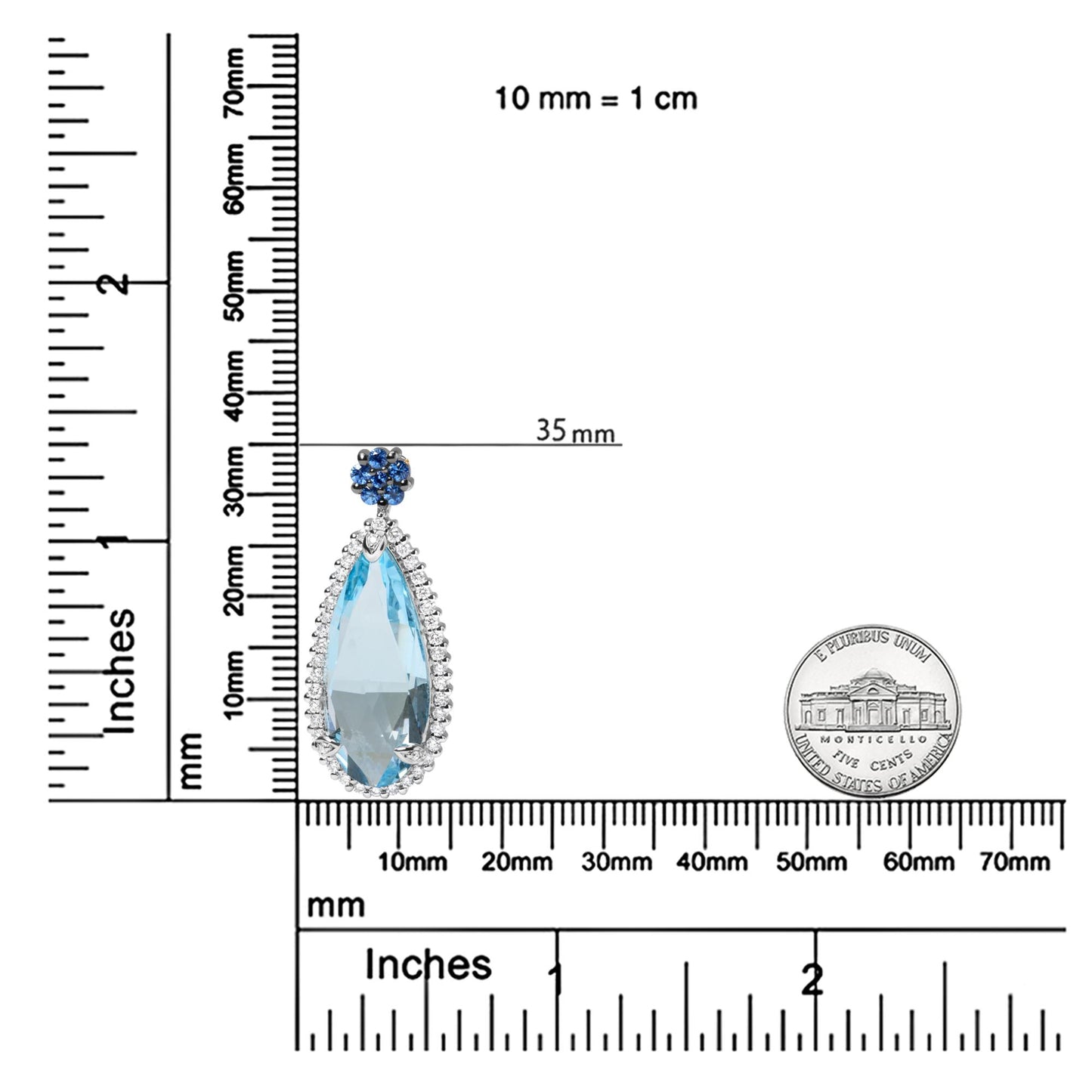 Close-up image of a white metal necklace pendant with a large pear-shaped blue gemstone surrounded by small white gemstones, topped with a cluster of round blue gemstones, displayed on a ruler for size reference.