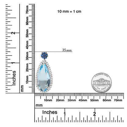 Close-up image of a white metal necklace pendant with a large pear-shaped blue gemstone surrounded by small white gemstones, topped with a cluster of round blue gemstones, displayed on a ruler for size reference.