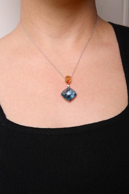 Necklace on a model featuring a white metal chain with a pear-shaped yellow gemstone, a small round white gemstone below it, and a cushion-shaped blue gemstone pendant, shot from the front.