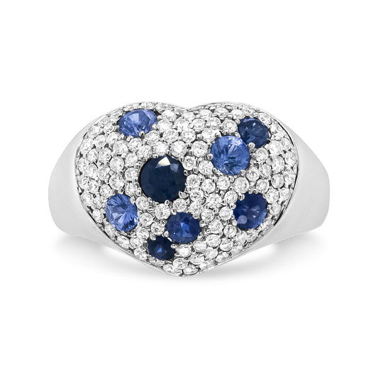 White metal heart-shaped ring viewed from the front, featuring round white gemstones in prong settings and multiple round blue gemstones in pave settings.