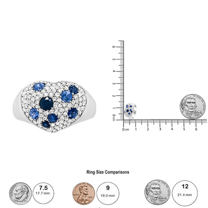 White metal ring with heart-shaped top viewed from the front, featuring numerous round white gemstones and scattered round blue gemstones in pave setting, shown next to a ruler and coins for size reference.
