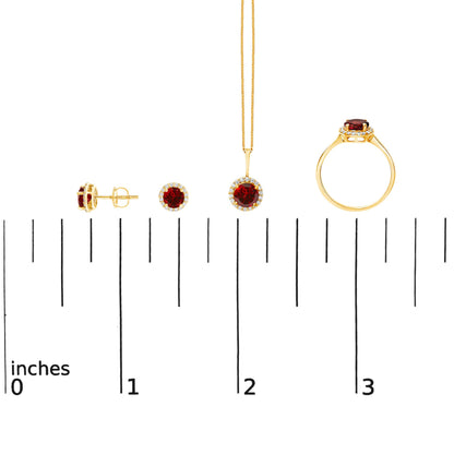 Set of yellow metal jewelry shown on a scale, including a pair of round red gemstone stud earrings with white gemstones surrounding, a matching pendant with a chain, and a ring with a round red gemstone center and surrounding white gemstones, displayed from a side and front angle.