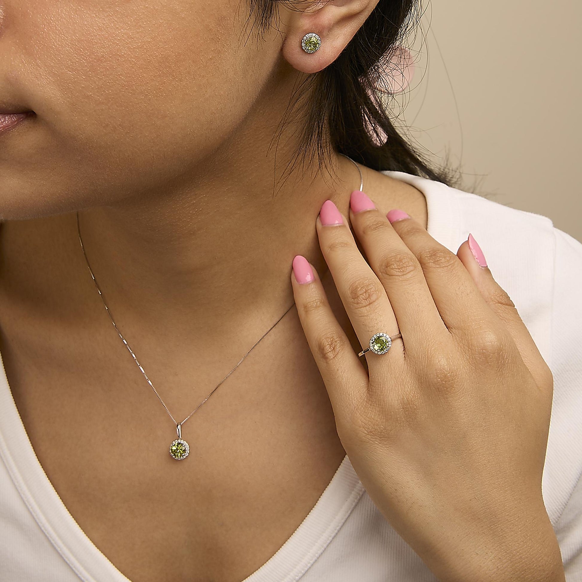 Close-up front angle of a model wearing a white metal jewelry set featuring round green gemstones surrounded by small white gemstones, including stud earrings, a pendant necklace, and a ring.