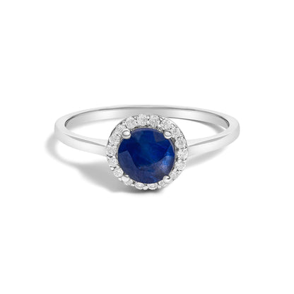 Close-up front angle of a white metal ring featuring a large round blue gemstone in a four-prong setting, surrounded by small round white gemstones in a shared prong setting.