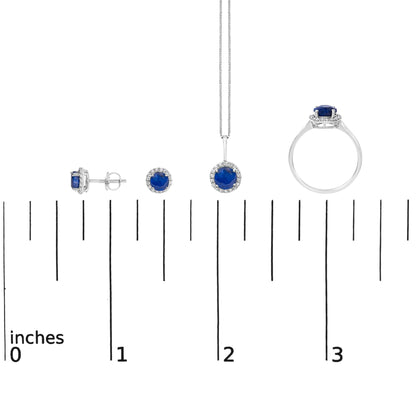 Jewelry set shown on a scale, consisting of stud earrings, a pendant necklace, and a ring, each featuring round blue gemstones surrounded by small white gemstones in shared prong settings, displayed from front, side, and top angles.