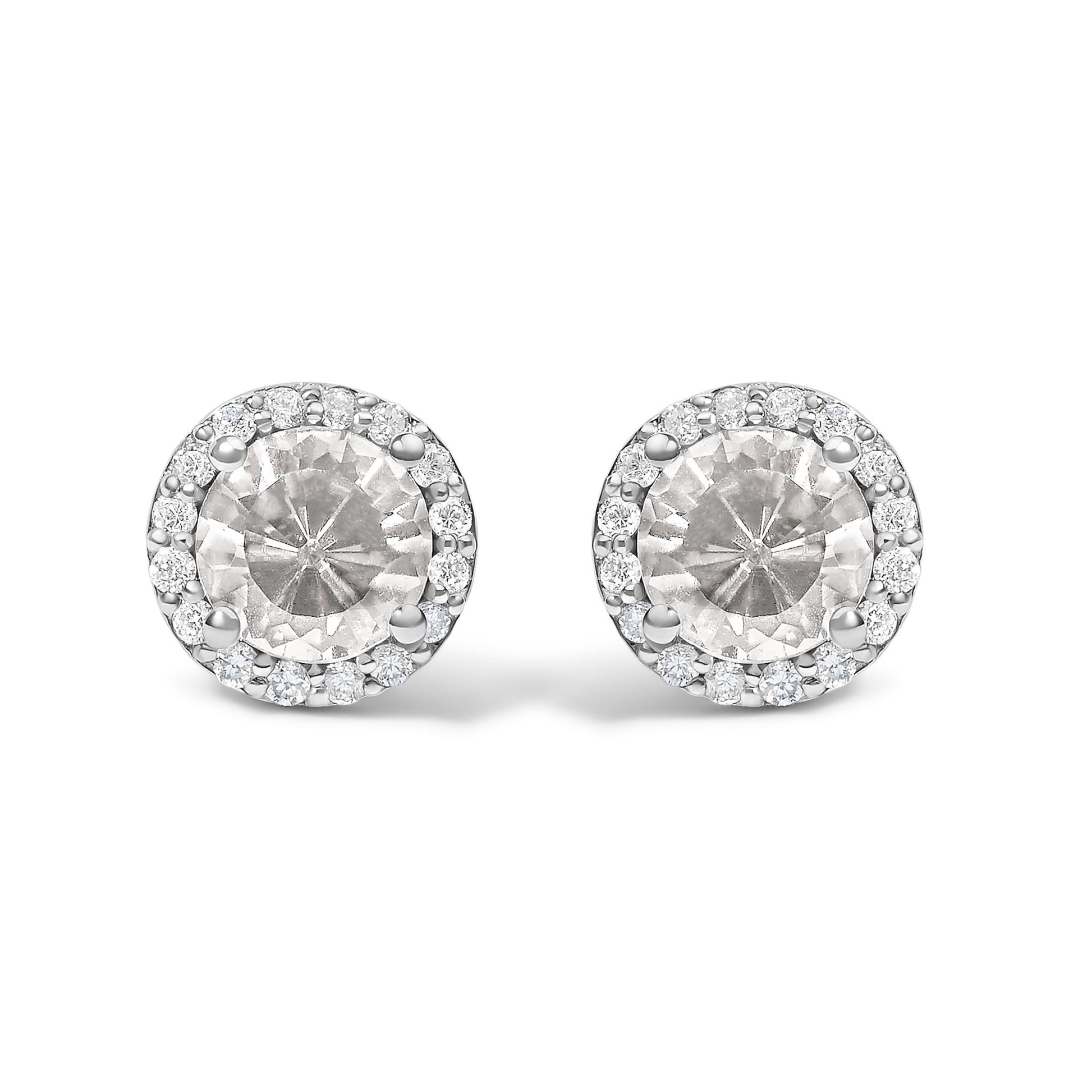 Close-up front view of a pair of round stud earrings featuring a central white round gemstone surrounded by a halo of small white round gemstones in shared prong settings. The earrings have a white metal color.