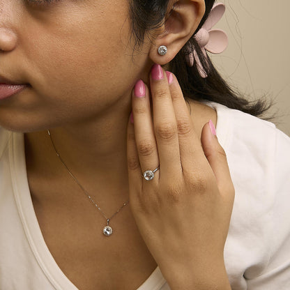 Set of white metal jewelry including round-shaped white gemstones surrounded by smaller round white gemstones in shared prong settings, shown worn on a model’s ear as earrings, finger as a ring, and neck as a pendant, front-facing angle.